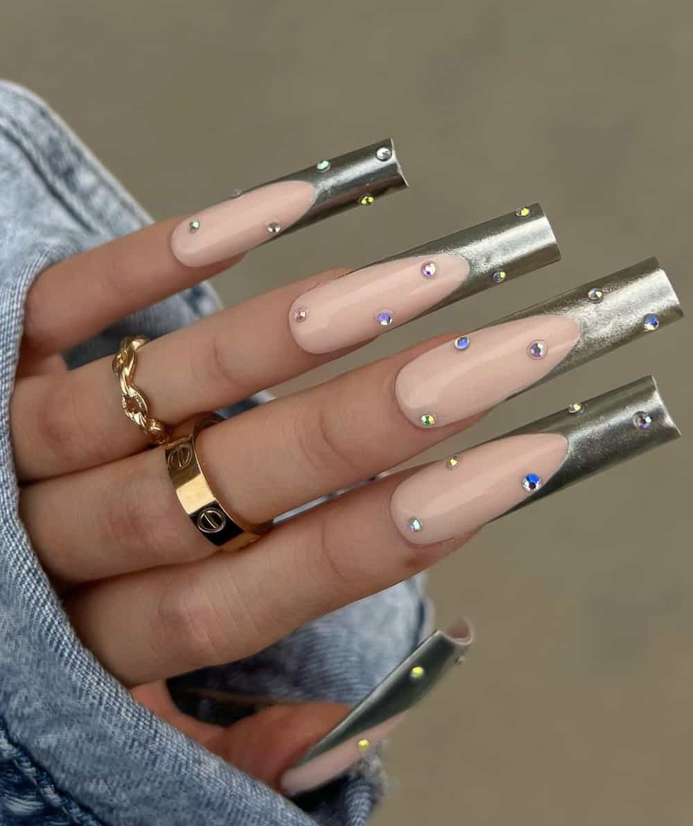 A hand with long square nails featuring silver French tips and gem accents