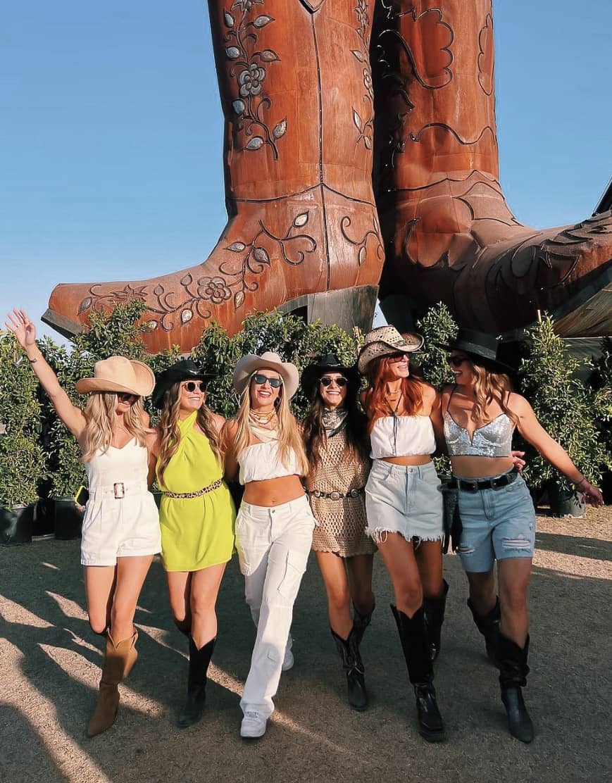 A group of six women at the Stagecoach music festival wearing chic country outfits with cowboy boots and cowboy hats