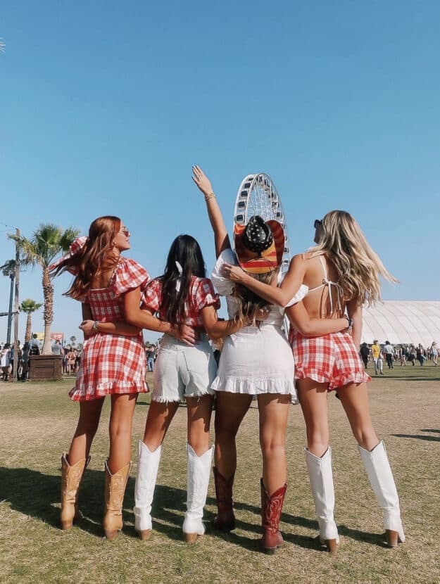 Four woman with their backs to the camera wearing red and white plaid and white festival outfits with cowboy boots