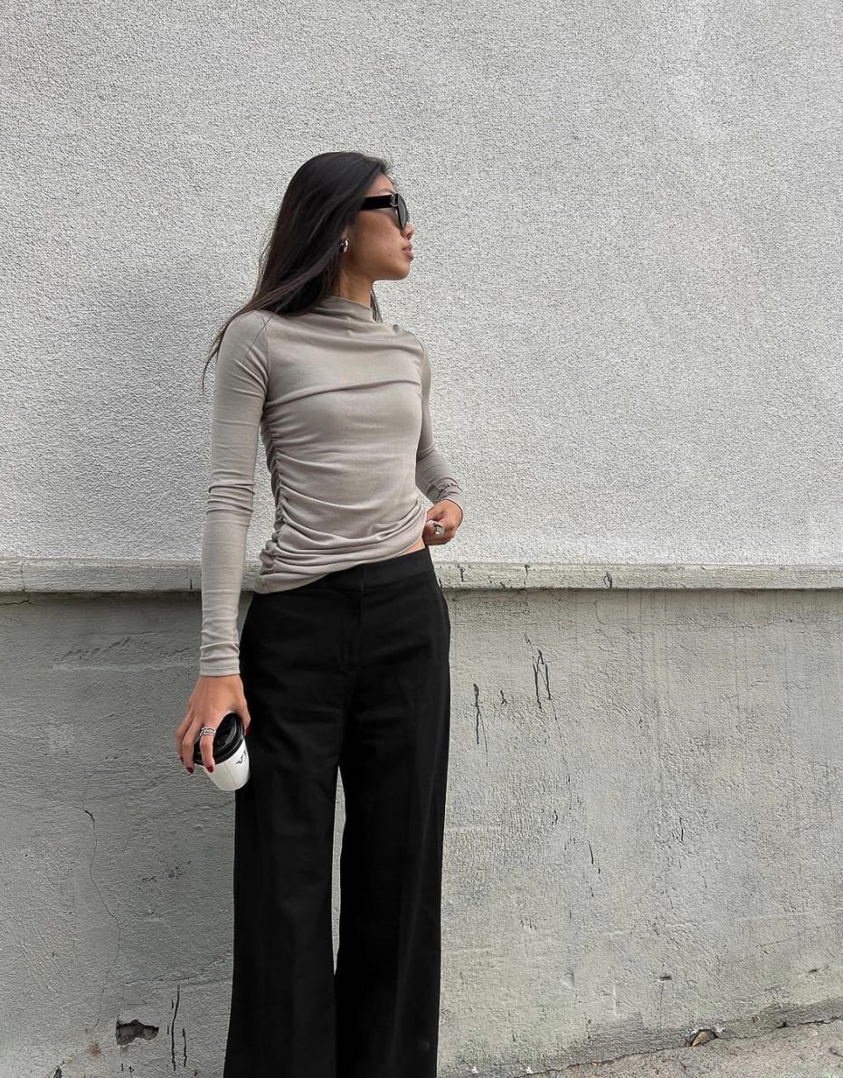 A woman wearing a long-sleeved grey shirt with a high neckline and black pants and sunglasses