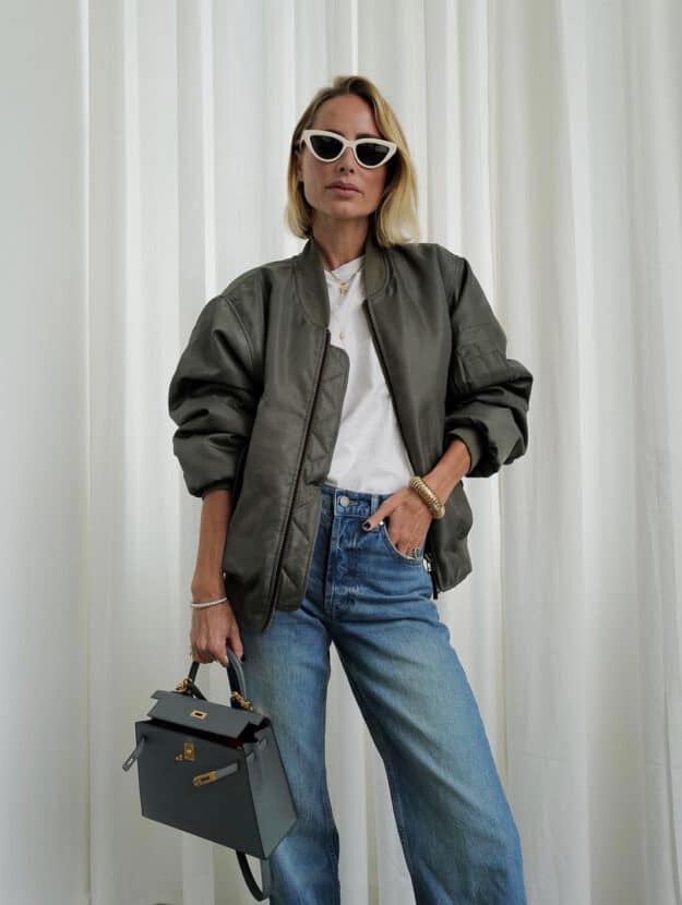 A woman wearing blue jeans with a classic white tee and a khaki green bomber jacket