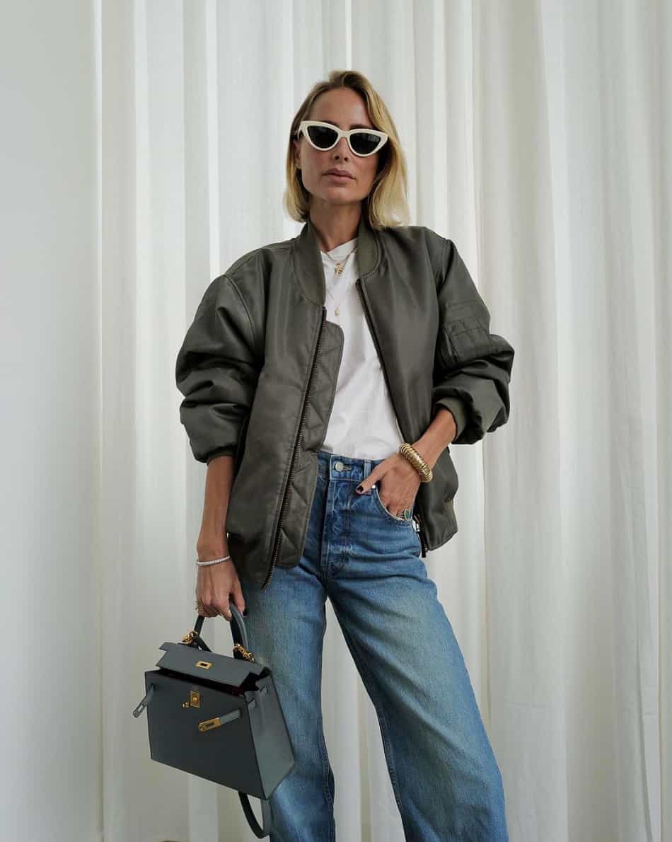 A woman wearing blue jeans with a classic white tee and a khaki green bomber jacket