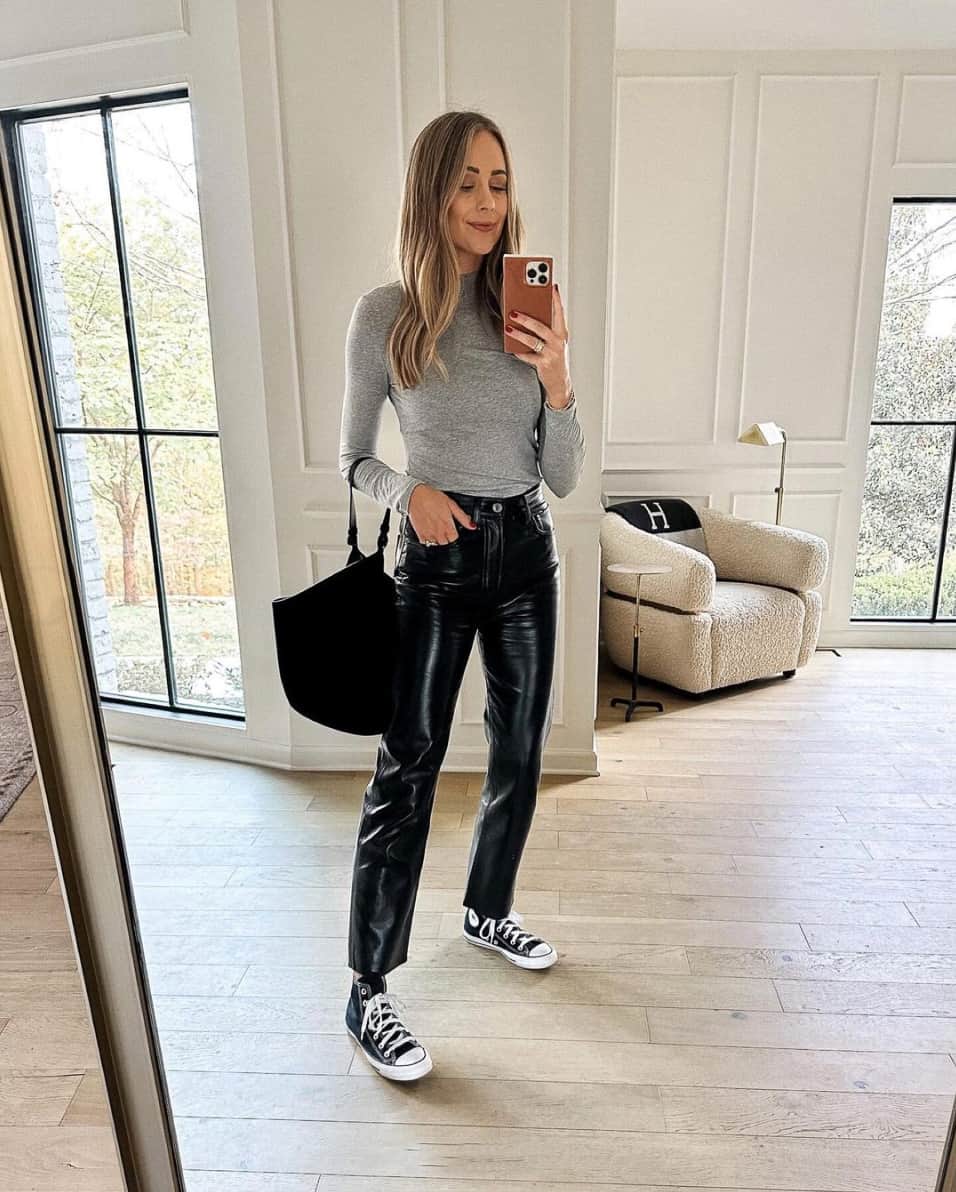 A woman wearing black leather pants with a long-sleeved grey shirt and Converse sneakers