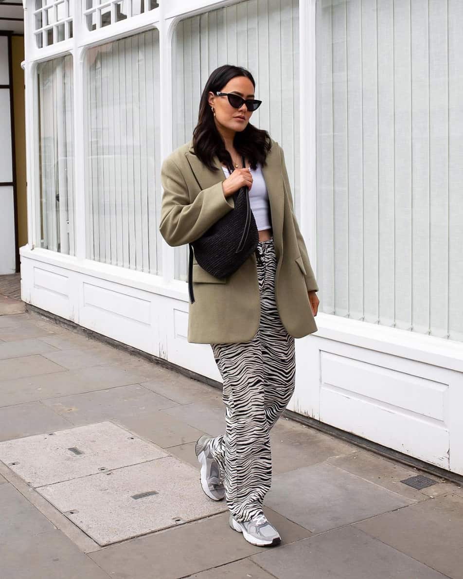 A woman wearing relaxed zebra print pants, a white crop top, and a beige blazer with trainers