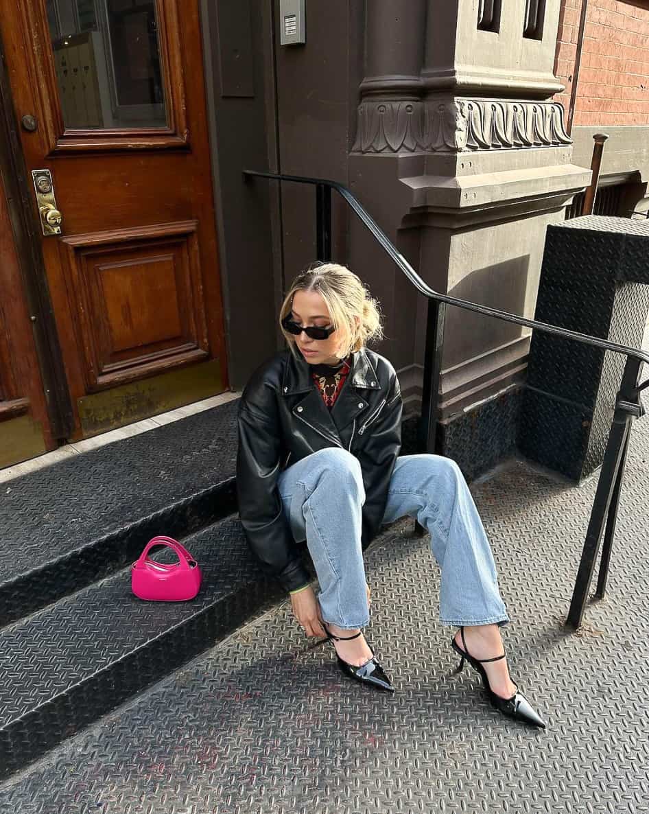 A woman wearing light blue jeans with a leather jacket and strappy black pumps