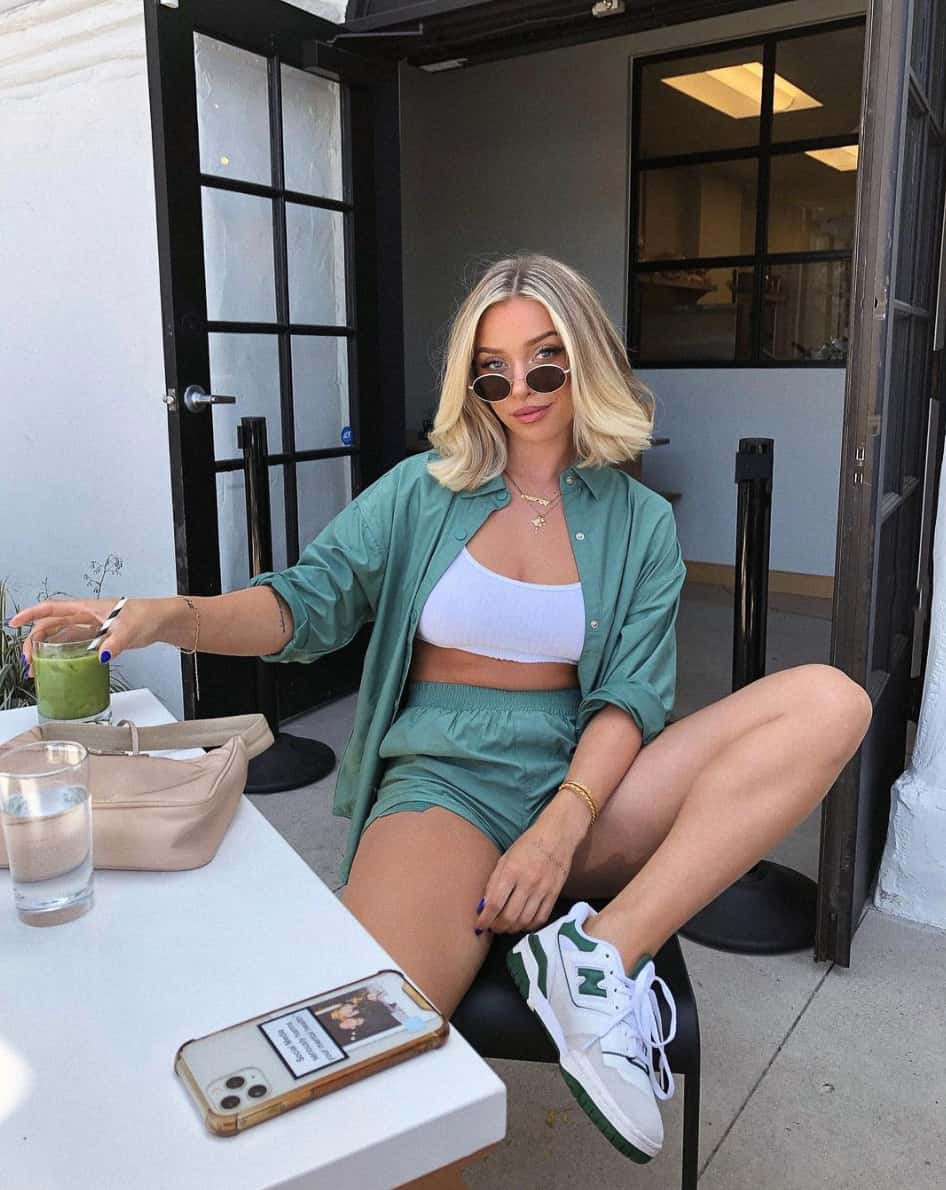 A woman wearing matching green shorts and a button-up shirt with a white bralette top and white and green sneakers