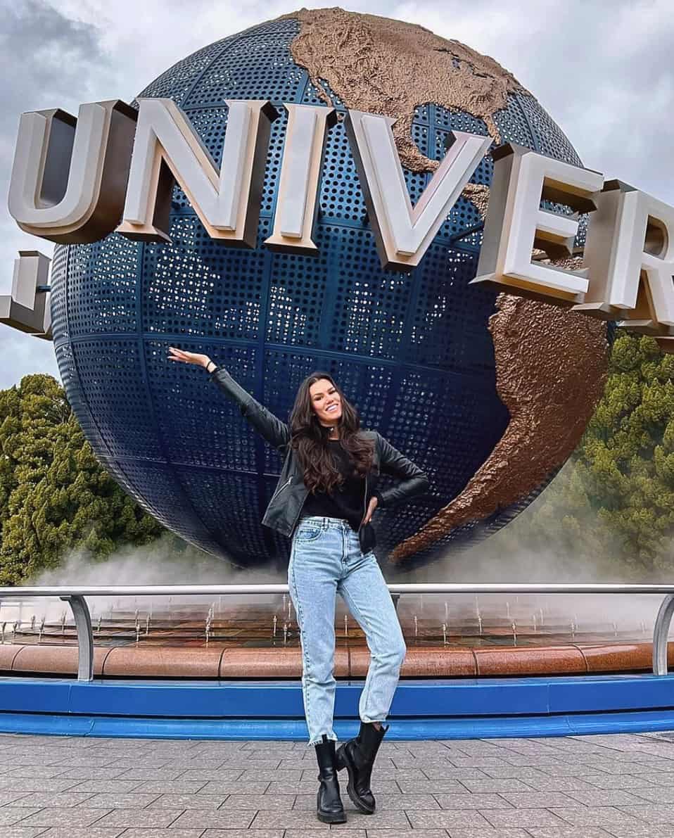 A woman wearing jeans, black Chelsea boots, a black shirt, and black leather jacket while standing in front of the Universal Studios globe