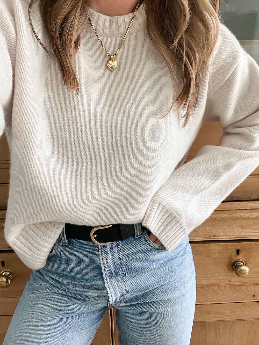 Christal wearing an ivory knit sweater from capsule wardrobe brand H&M with a black belt and blue jeans