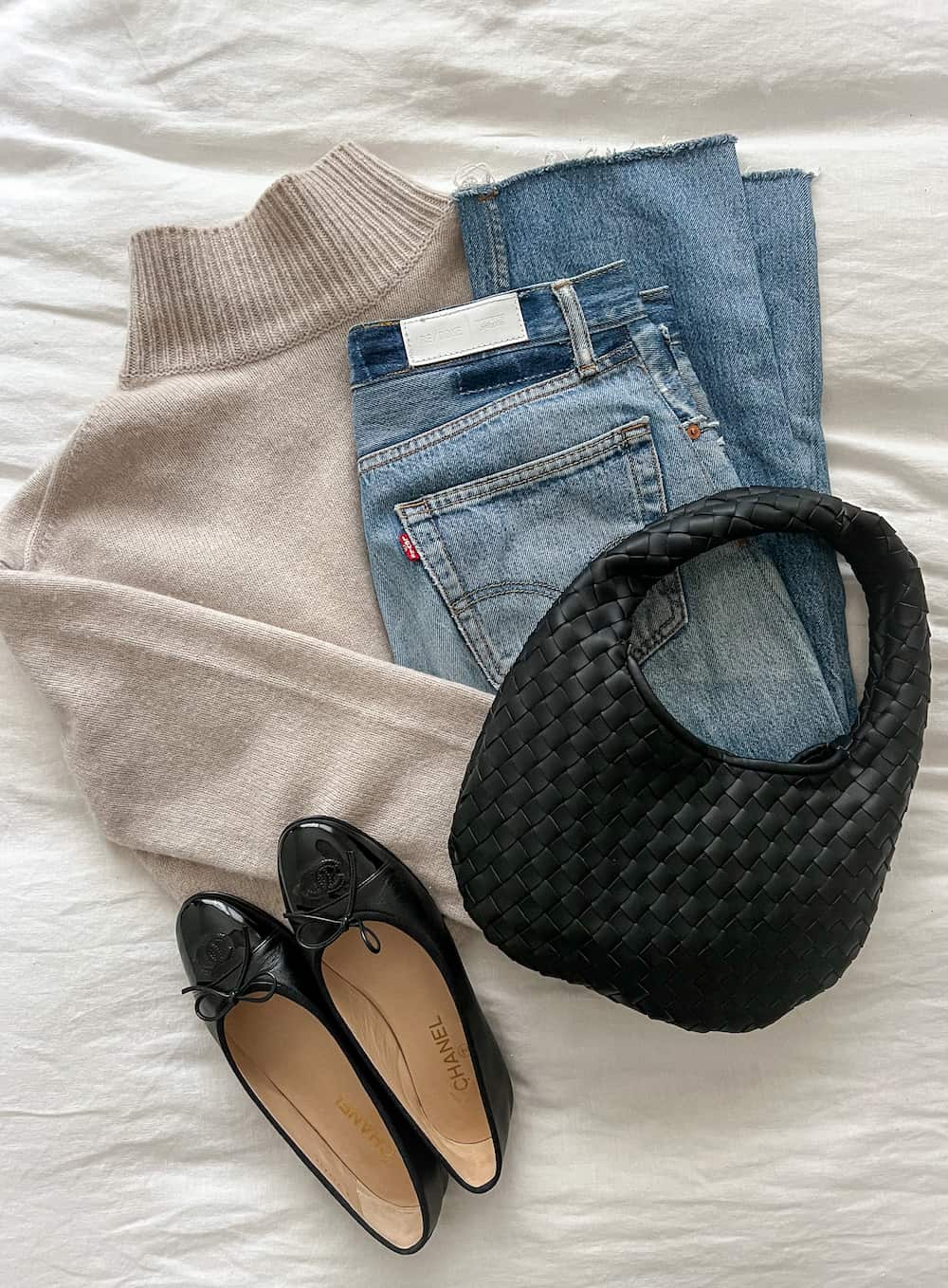 outfit flat lay with capsule wardrobe pieces including a beige turtleneck, jeans, black ballet flats and an Oak & Fort woven black bag