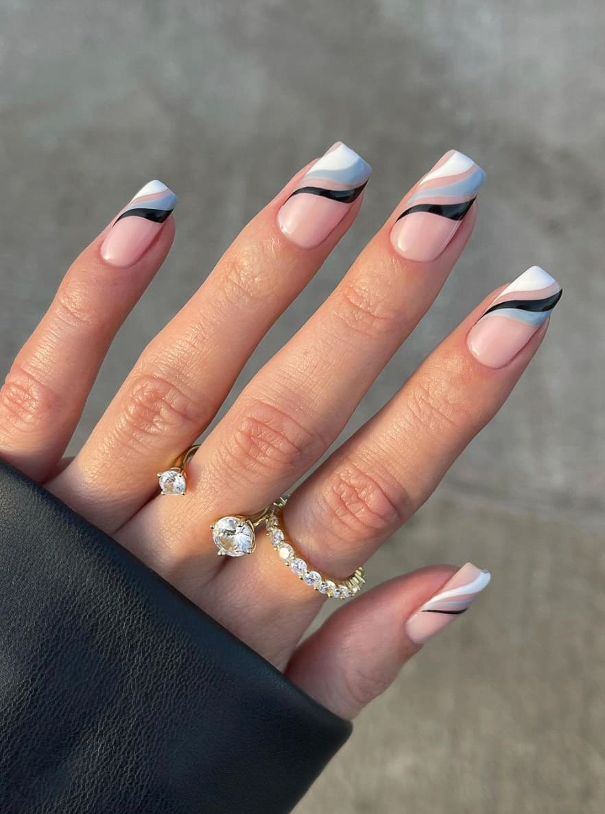 A hand with long square nails featuring a glossy nude base and white, grey, and black swirls