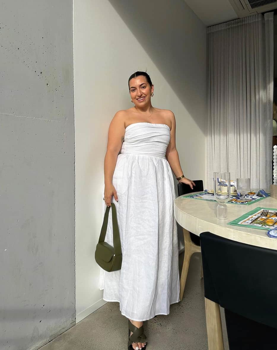 A woman ready for happy hour, wearing a strapless white maxi dress with khaki green sandals and a handbag
