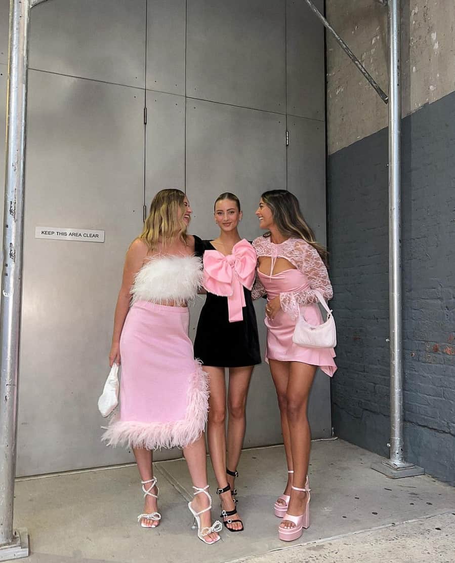 Three woman ready for a Harry Styles concert outfits, featuring pink dresses, feathered trim, lace, and bow details
