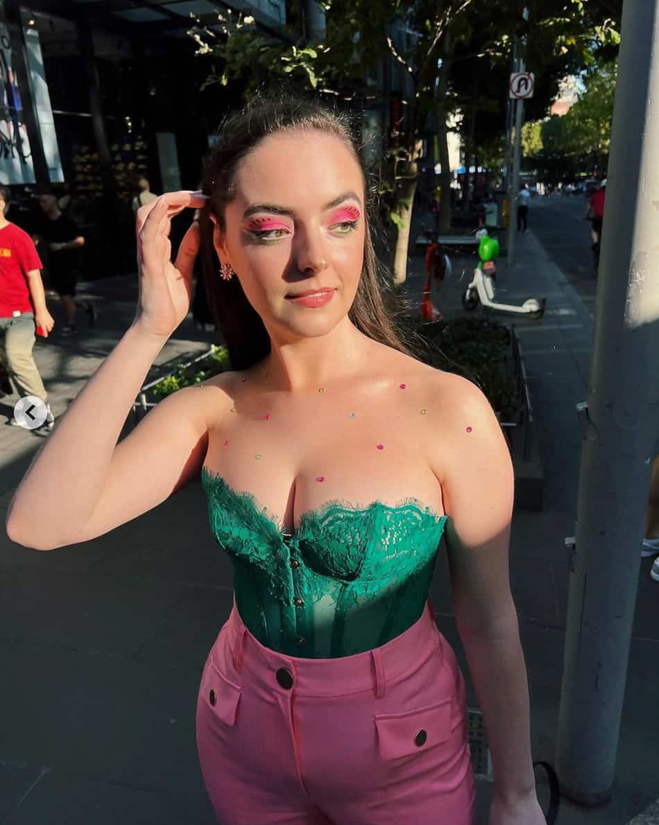 A woman wearing a kelly green lace corset top paired with pink bell bottom pleated pants