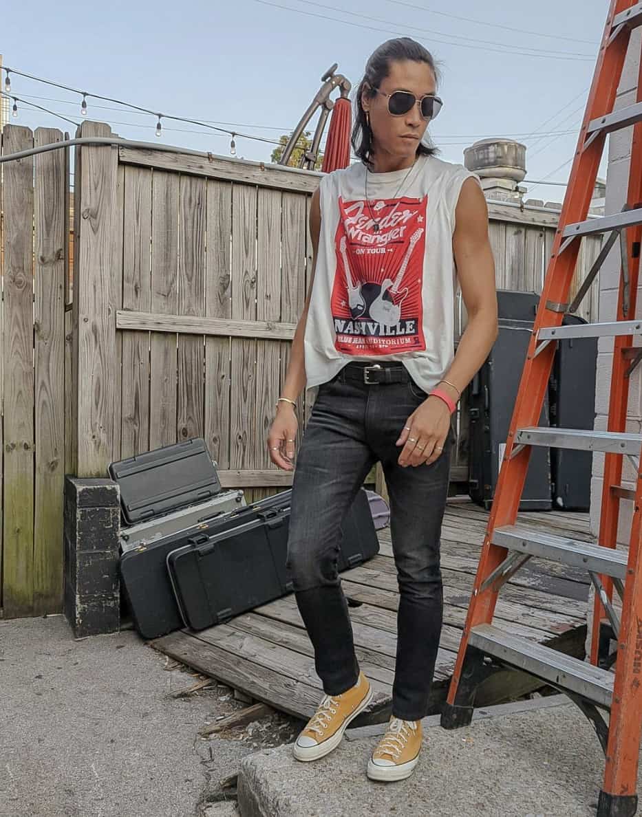 A man wearing black jeans, a graphic tee, and yellow Converse shoes