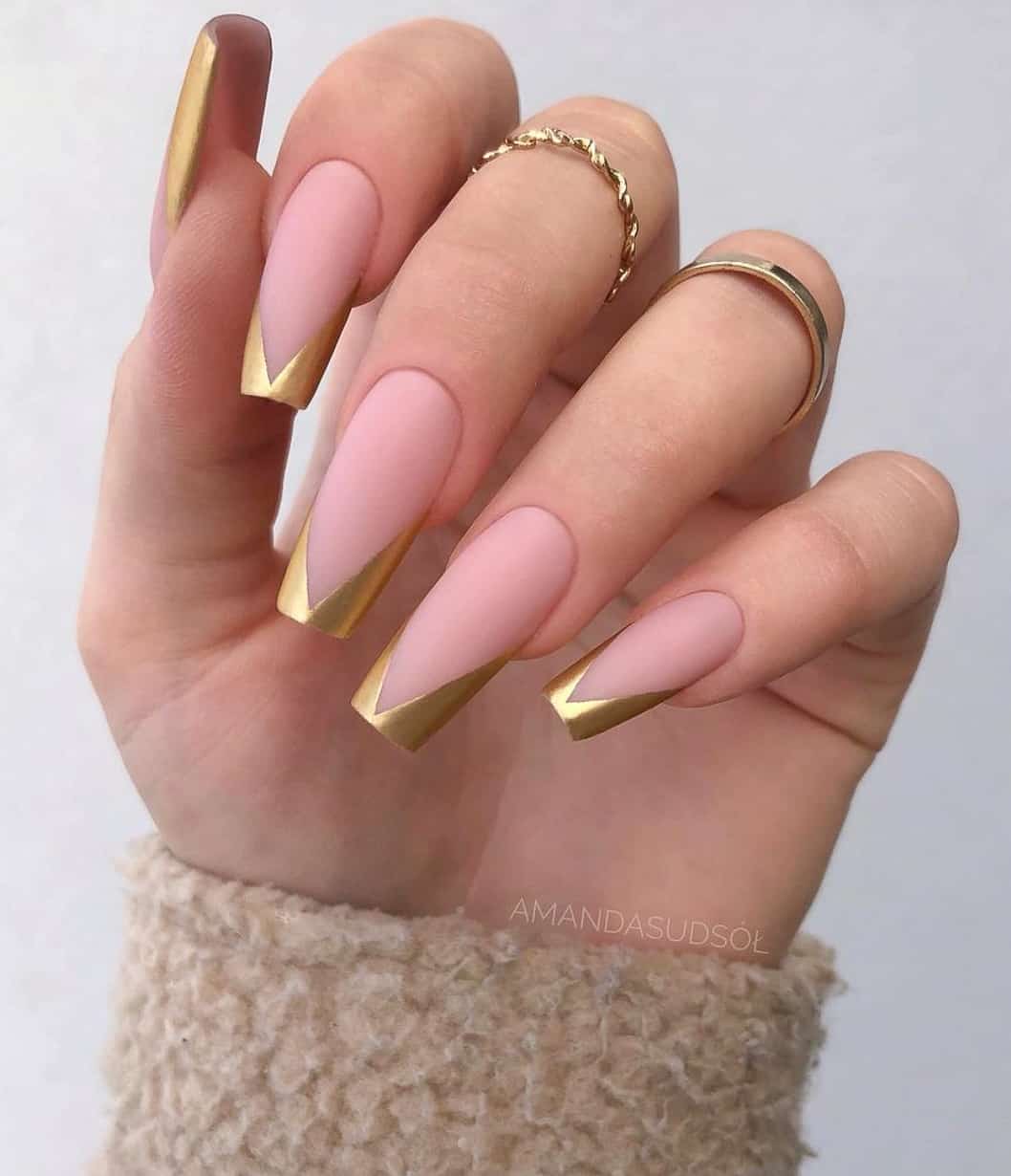 A hand with nude pink matte coffin nails featuring slanted gold French tips