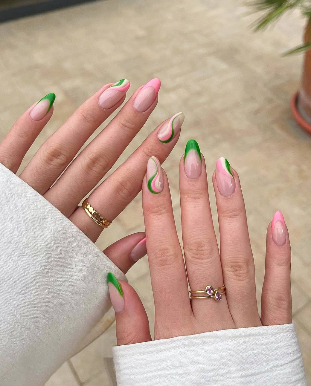 A hand with medium-length nude almond nails with pink and green French tips and white, pink, and green wavy accents