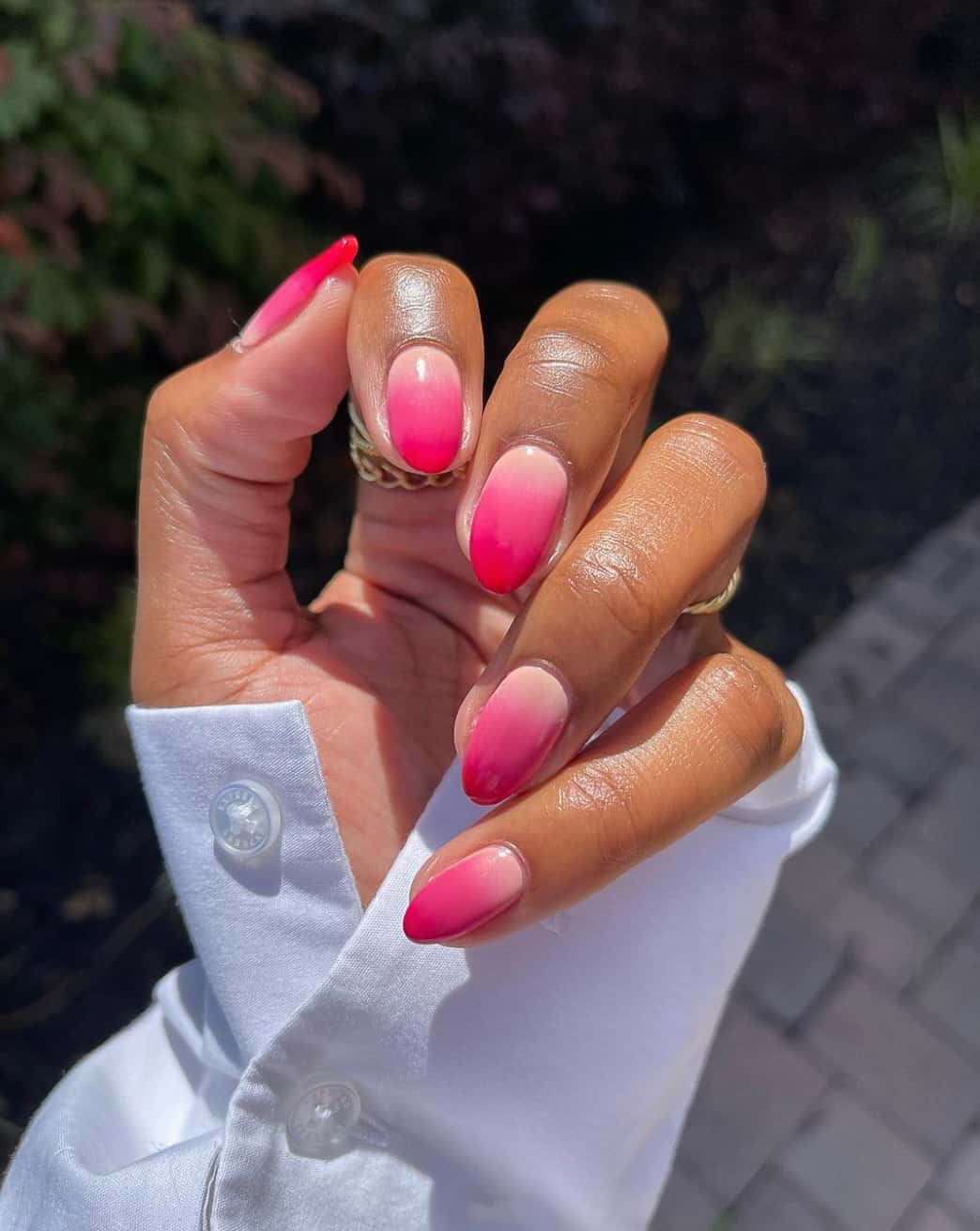 A hand with medium almond nails featuring a light pink to red ombre