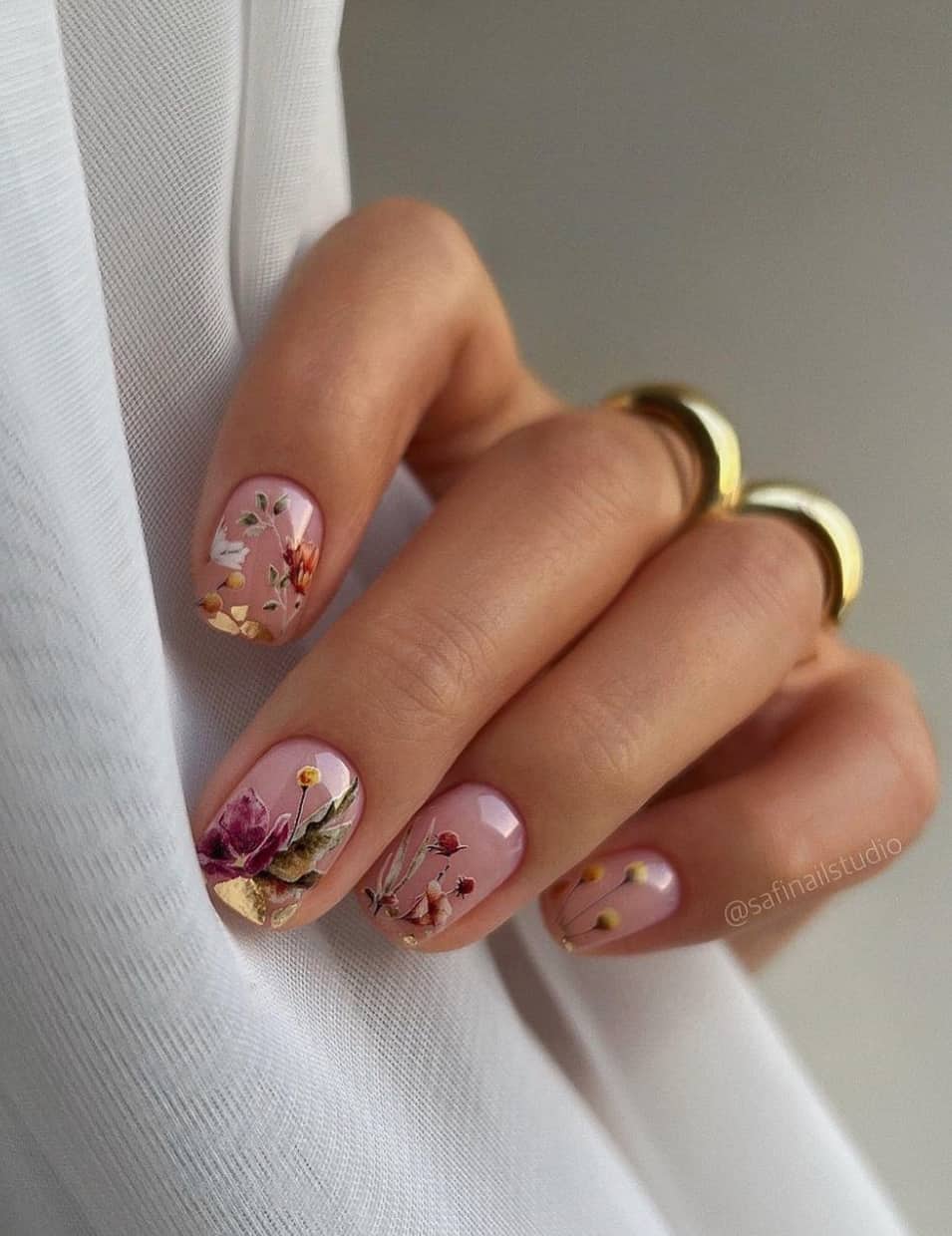 A hand with short square nails with a light pink polish and intricate floral art