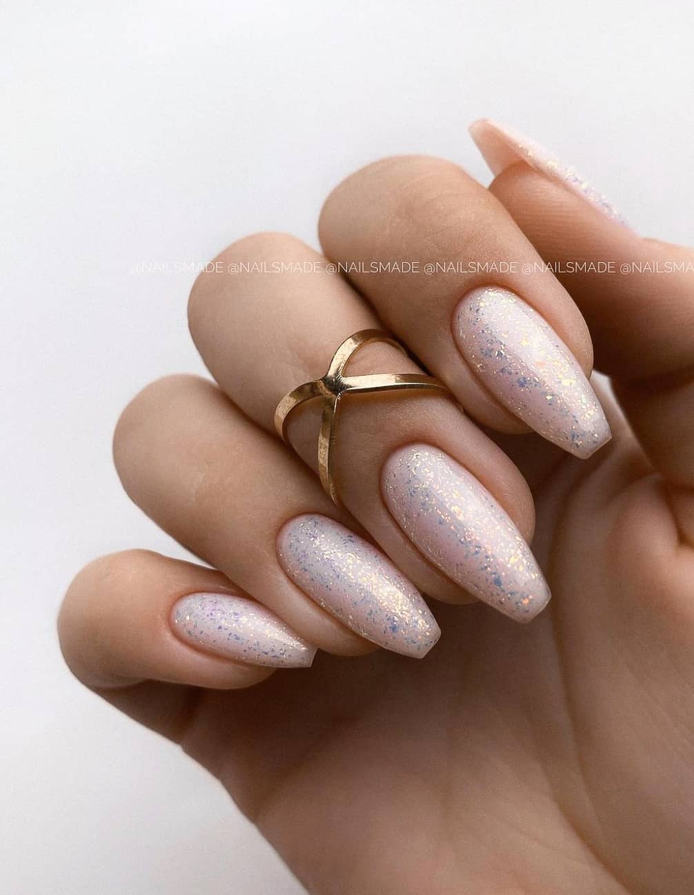 A hand with coffin nails featuring a light pink nail polish and iridescent glitter