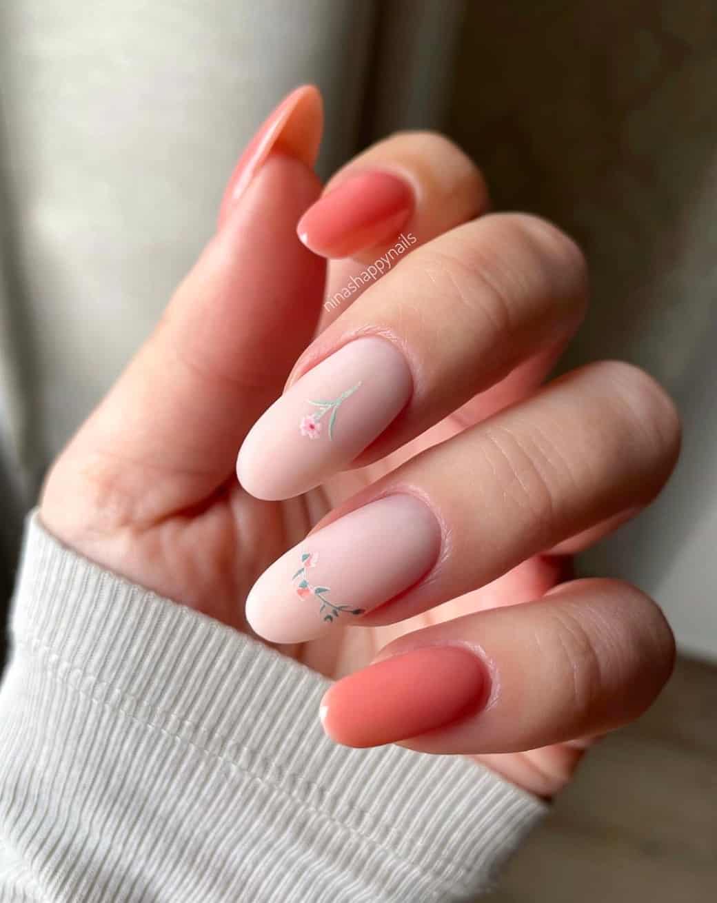 A hand with glossy pink almond nails and light pink matte accent nails with floral art