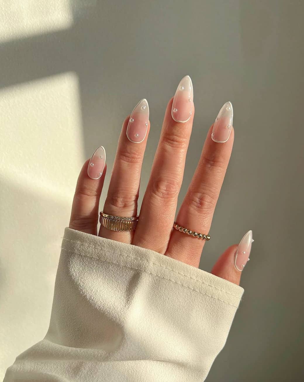 A hand with medium length nude stiletto nails with pearl accents