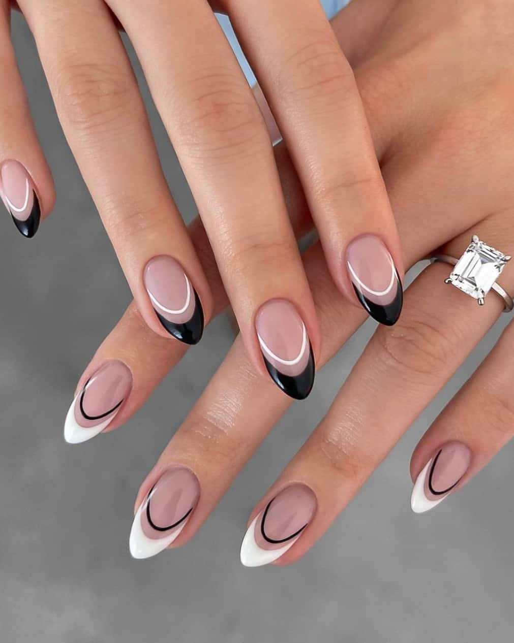 Two hands with almond nails featuring black French tips and white accent lines on one hand and white French tips with black accent lines on the other