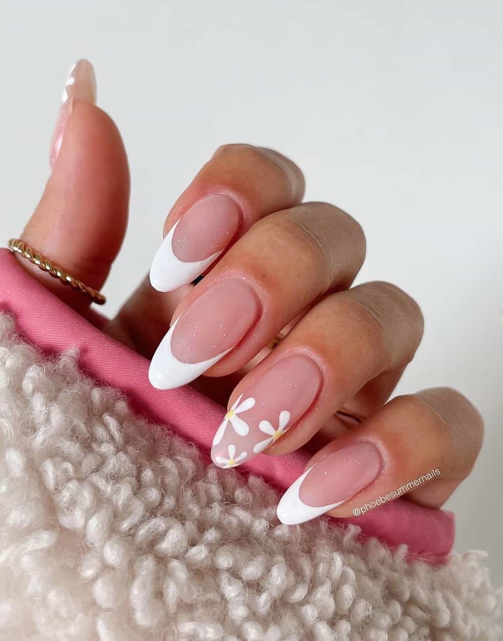 A hand with long almond nails with white French tips and accent nails with white flowers