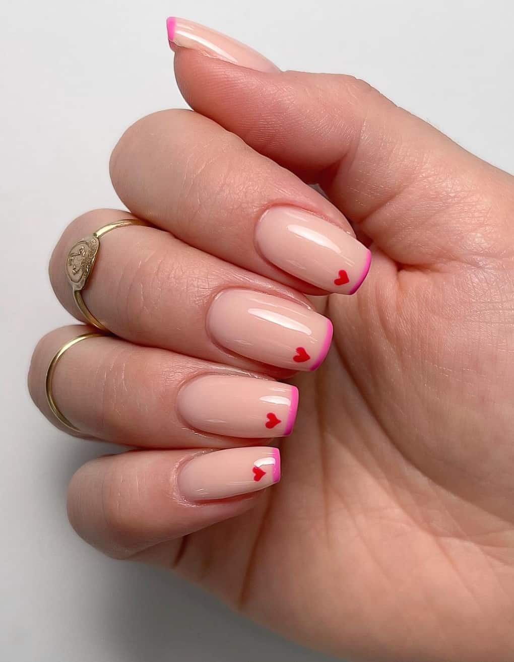 A hand with medium length square nails with pink French tips and tiny red hearts
