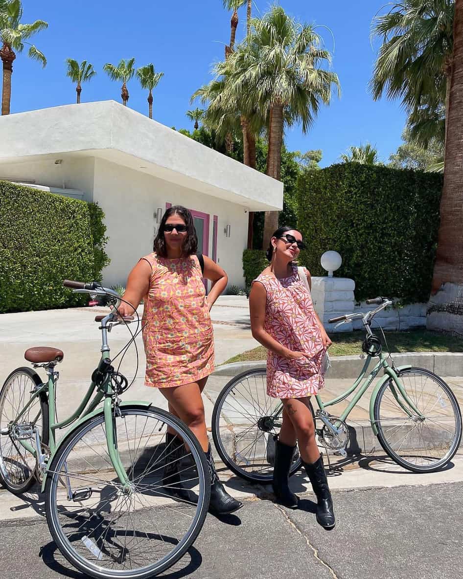 Two woman riding bikes in Palm Springs with 70s styles patterned dresses and skirt sets with black cowboy boots
