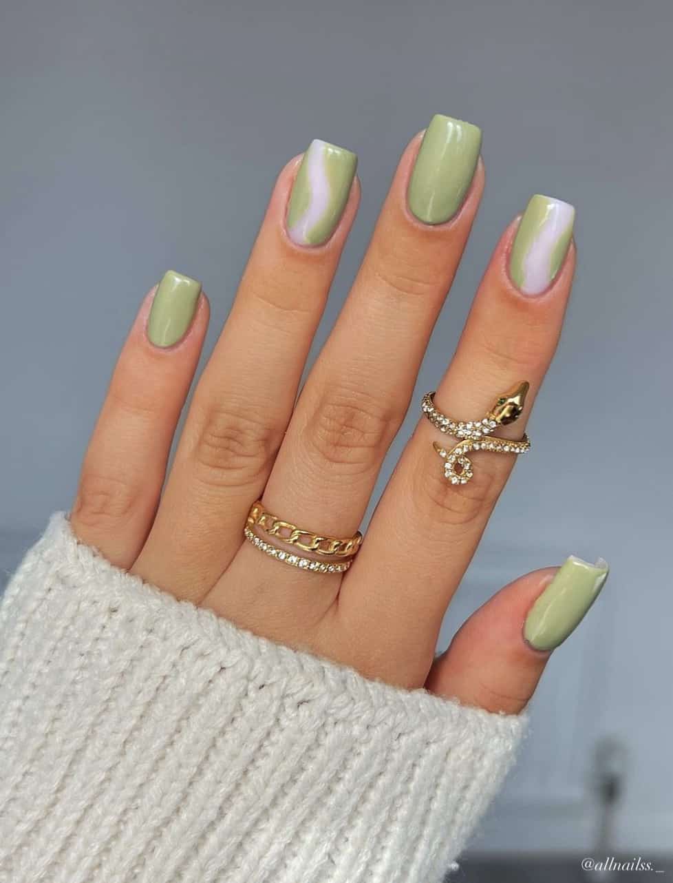 A hand with short square nails painted a light green shade with green and milky white wave accent nails