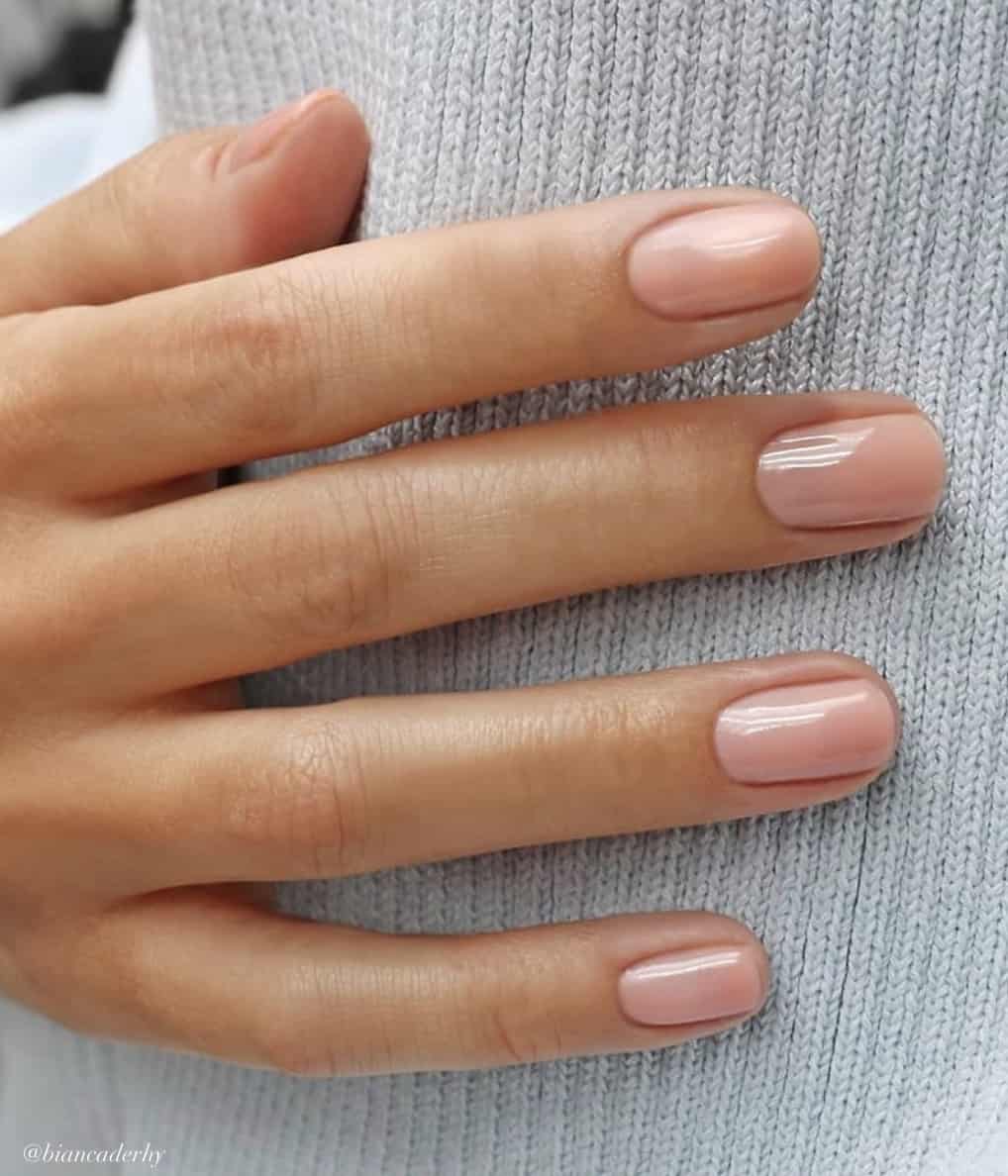 A hand with short round nails painted in a glossy nude polish