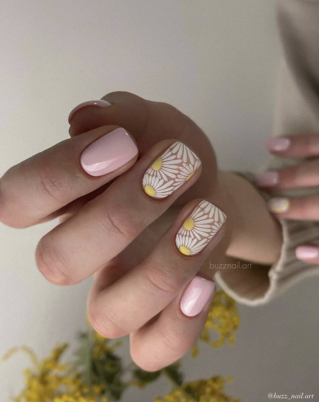 A hand with short square nails painted a light pink and accent nails with white daisy nail art