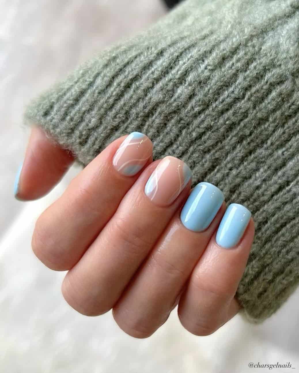 A hand with short squoval nails painted a baby blue color with nude accent nails with a baby blue and white nail design