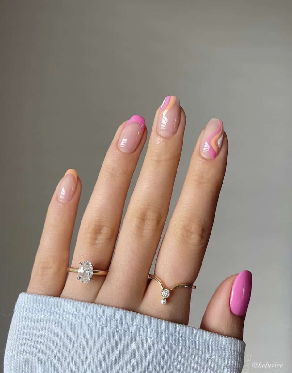 A hand with short square nails painted in glossy nude with orange and pink French tips and waves with a solid colored pink accent nail