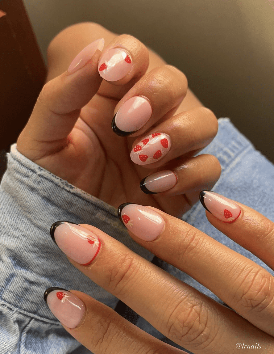 A hand with short round nails in a nude polish with black French tips and strawberry nail art