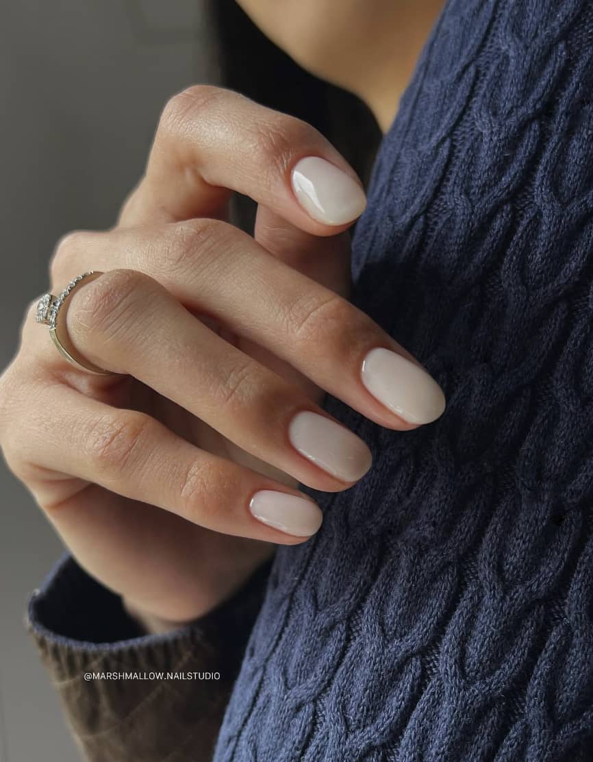 A hand with short round nails painted in a milky white nail color