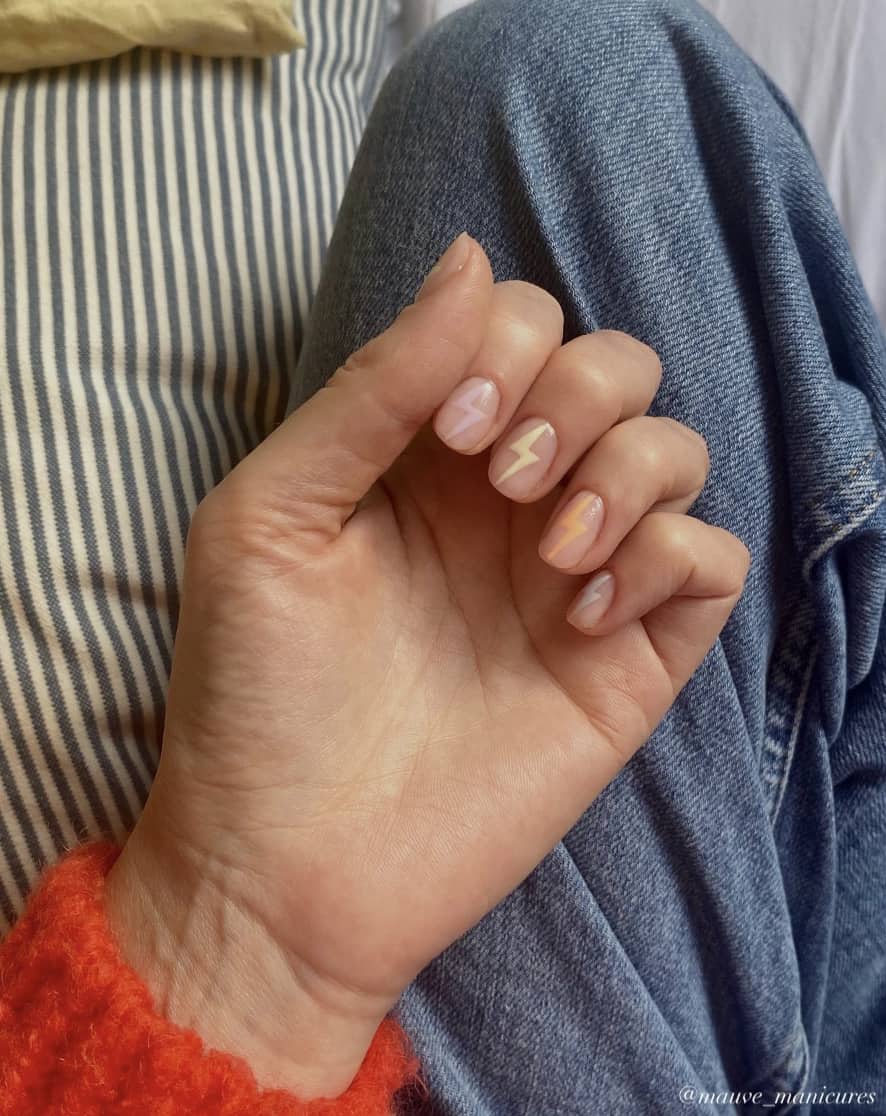 A hand with short squoval nails painted a nude color with gradient pastel lightning bolts