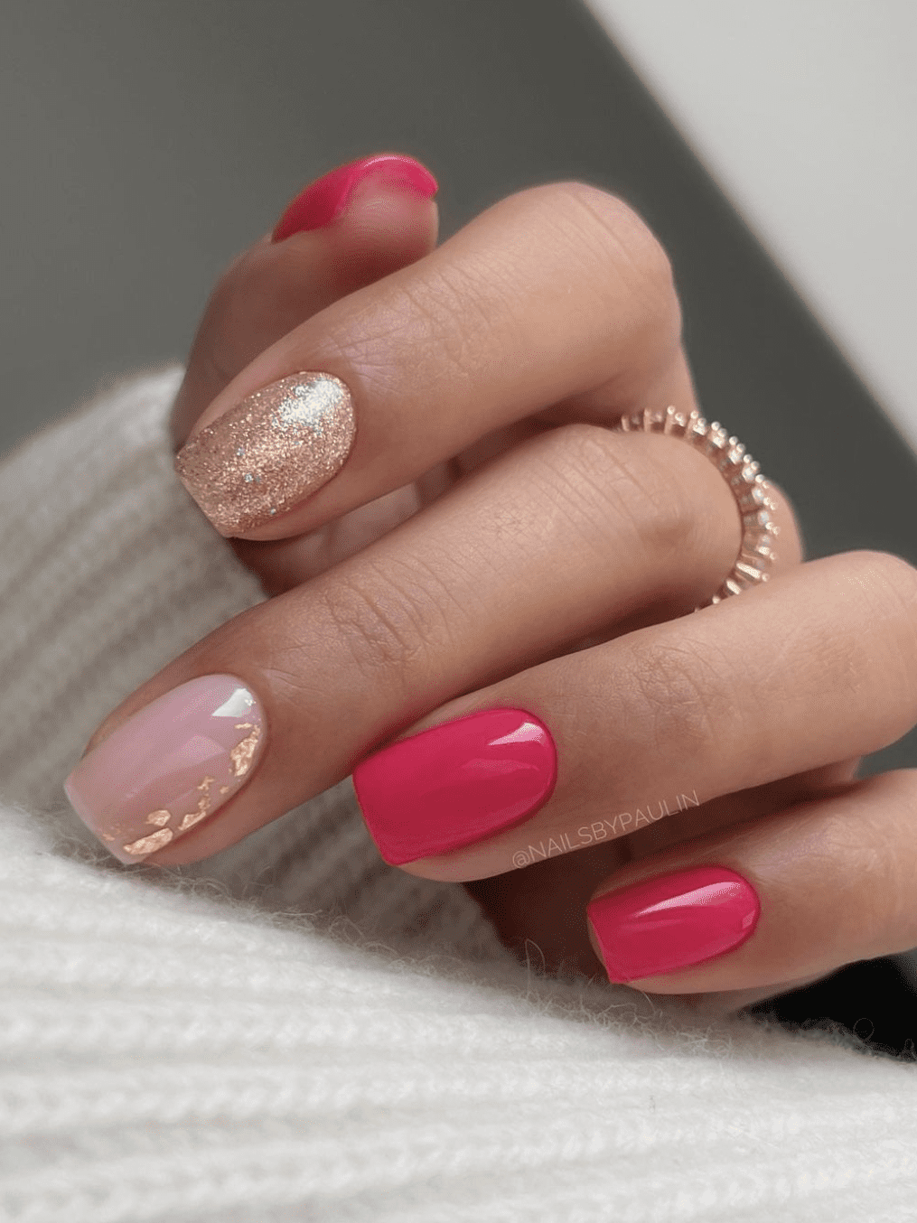 A hand with short square nails painted in a bright pink nail polish and accent nails with nude pink polish and gold flakes and solid gold glitter