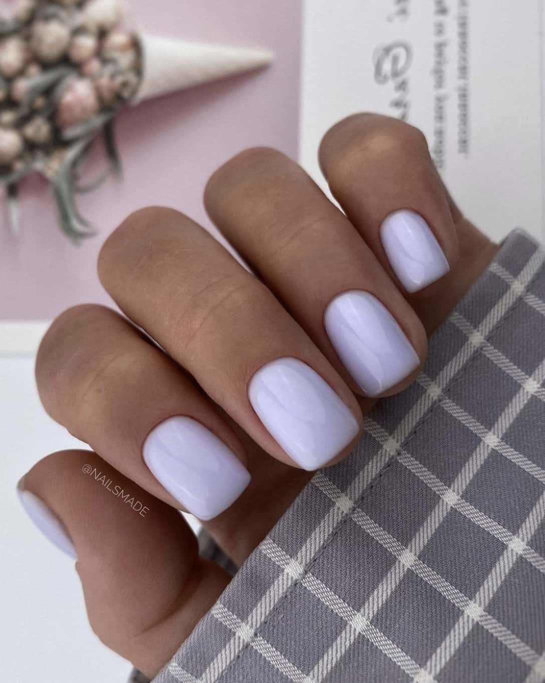 A hand with short square nails painted with pastel lilac nail polish