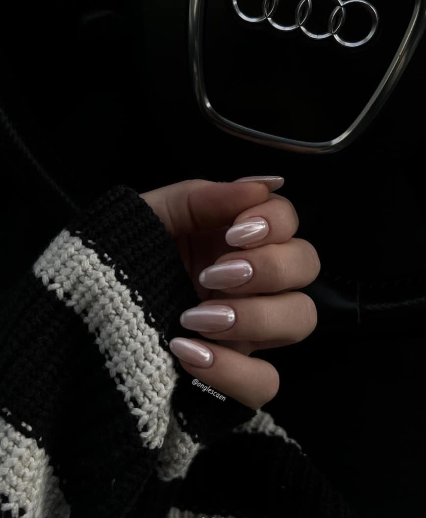 A hand with short round nails painted a light pink with a pearly finish