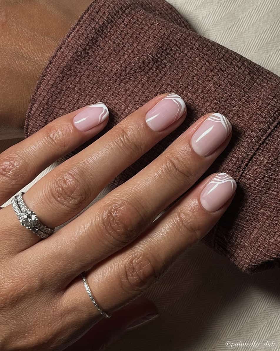 A hand with short squoval nails with white line French tips and a glossy finish
