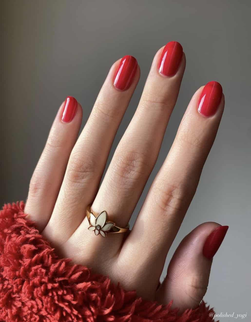 A hand with short round nails painted in a solid bright red polish