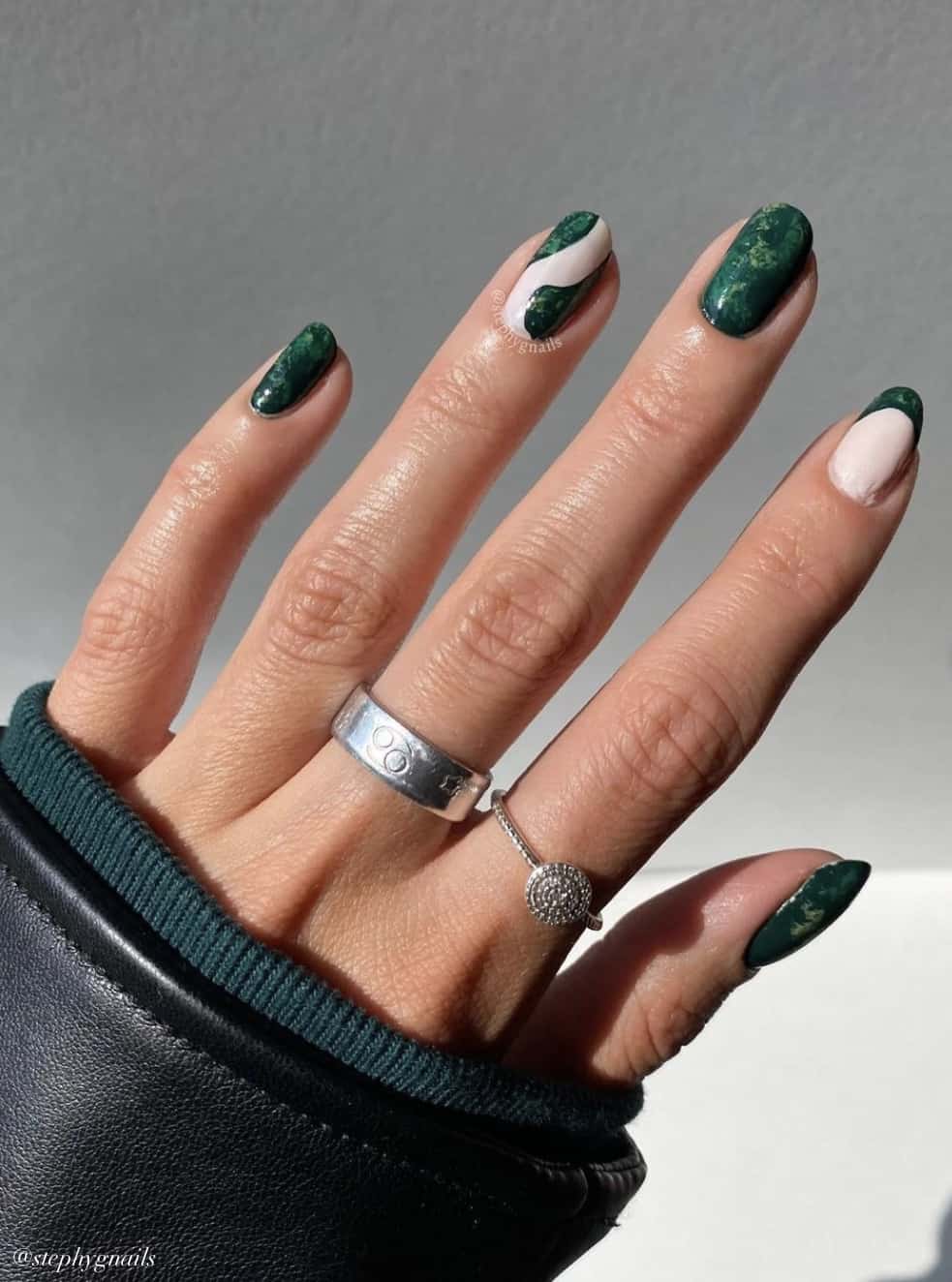 A hand with short round nails with green solid-colored nails and two accent nails with green French tips and waves