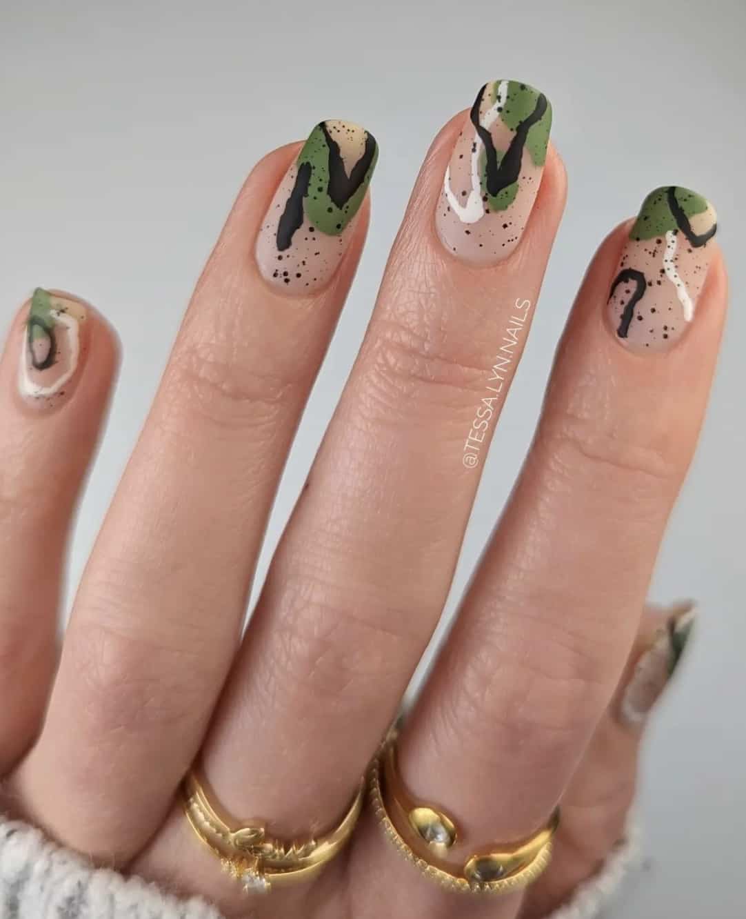 A hand with short square nude nails with black, white, and green abstract nail art with a matte finish