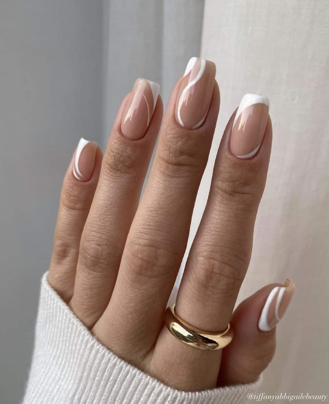 A hand with short square nails painted with nude polish and white wave accents with a glossy finish