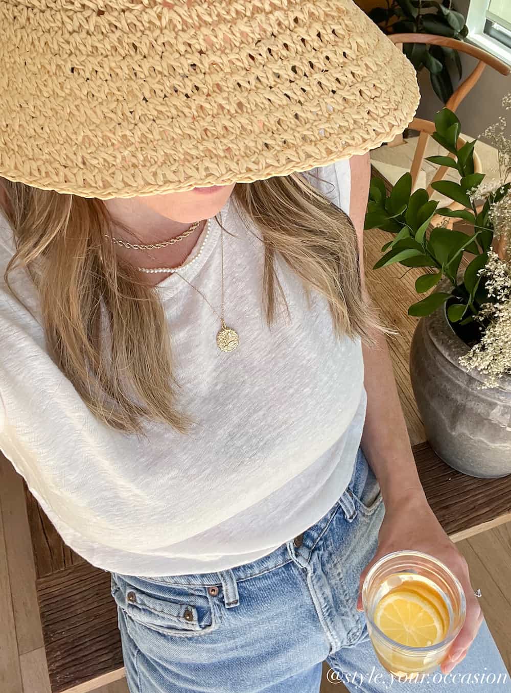 image of a woman wearing a raffia hat, white linen tank top, and blue jeans as part of a summer capsule wardrobe