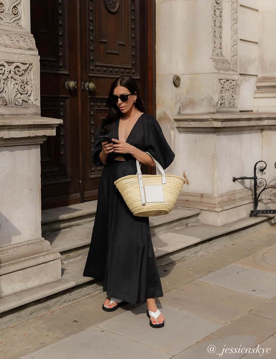 Woman wearing a stylish summer outfit with a black midi sun dress, basket tote bag, and white sandals