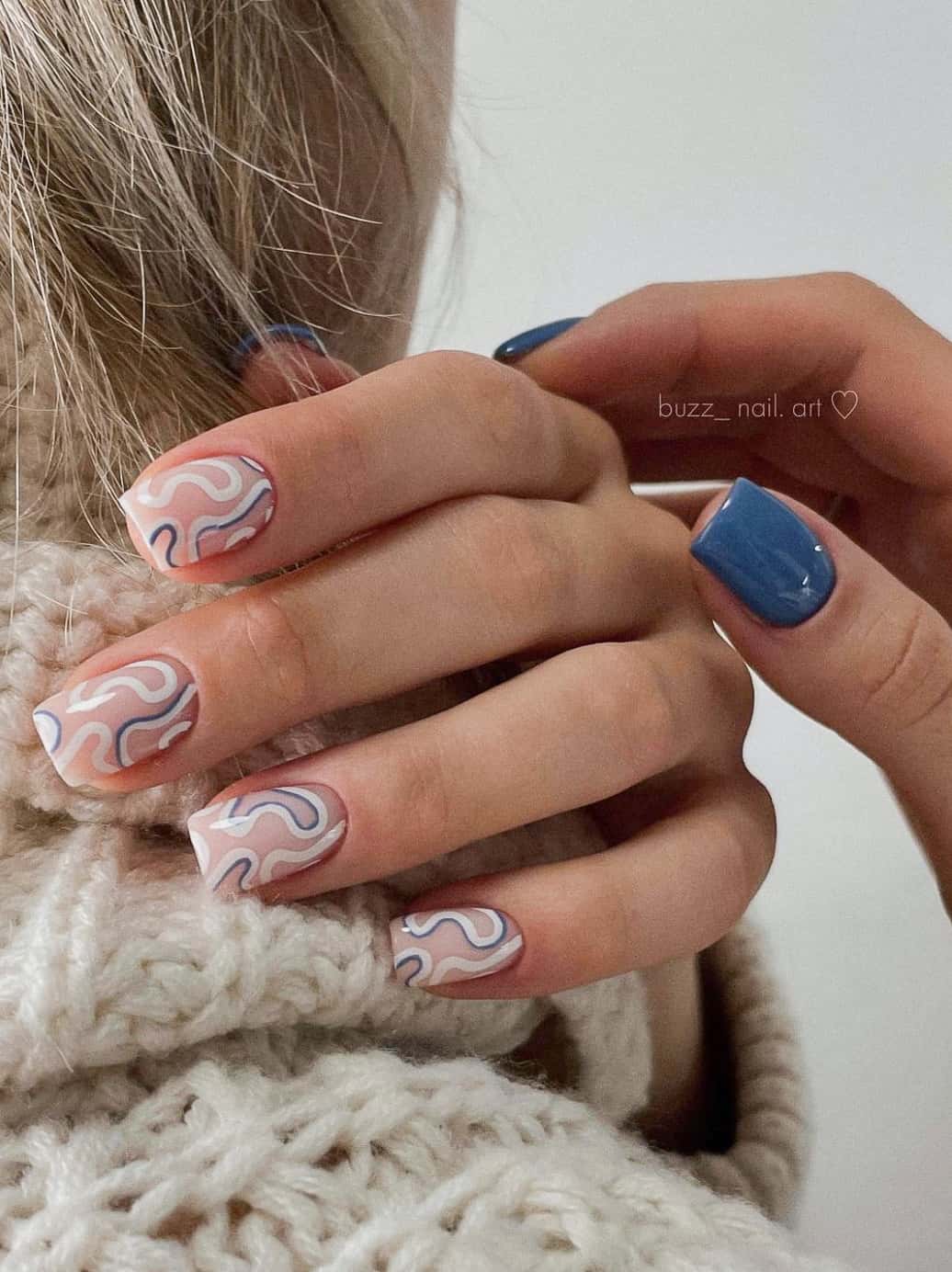 Two hands, one with solid blue polished nails and the other with a nude base and white and blue swirls