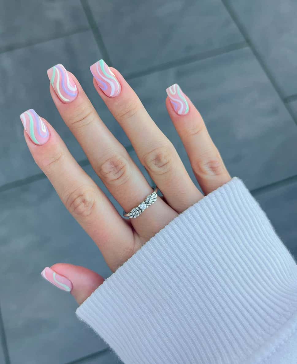 A hand with medium length square nails featuring pastel rainbow swirl accents