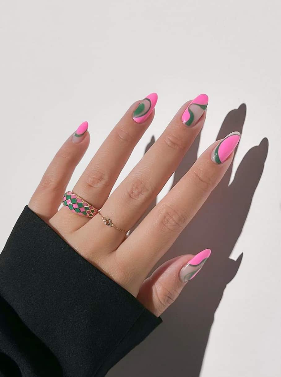 A hand with medium round nails featuring a glossy nude base and pink and dark green swirl accents